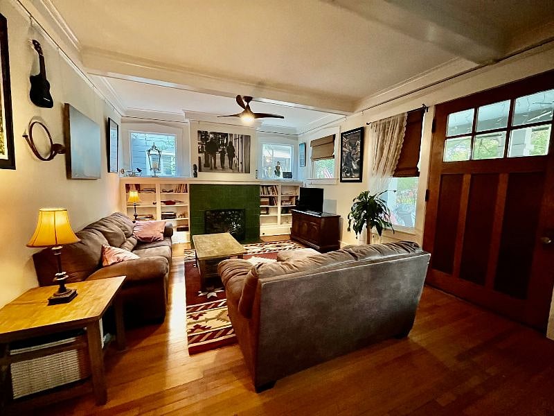 A large living room with tall coffered ceilings features couches, a flat screen Internet TV, decorative fireplace, small tables and built-in Craftsman style bookshelves.