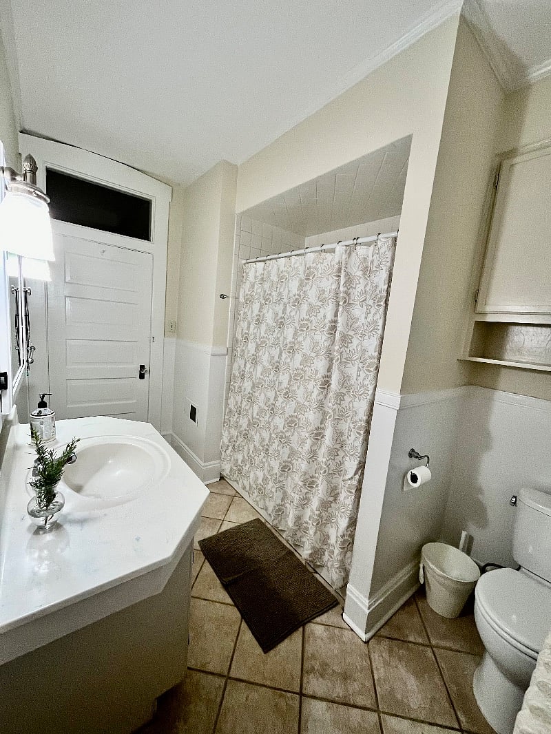 Central bathroom features toilet, sink, bath and shower combo, a linen closet and ample shelving.
