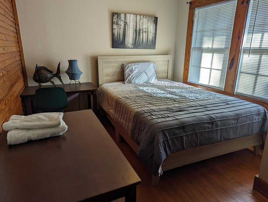 Bedroom 1, queen bed, desk, chest of drawers, closet with wire shelving. Windows look out onto the side yard and side patio.