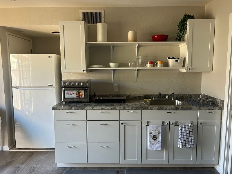 Kitchenette with full sized fridge, large sink, counter top two burner hot plate and combination air fryer/toaster oven. 