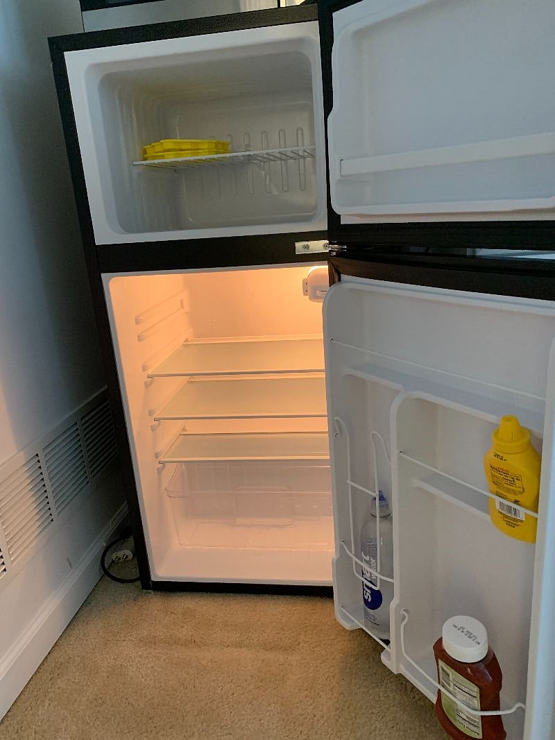 Small refrigerator and freezer inside efficiency room with complimentary ketcup, mustard, and bottled water.