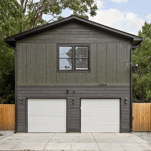 Modern two-story garage apartment with a sleek black exterior and dual white garage doors.