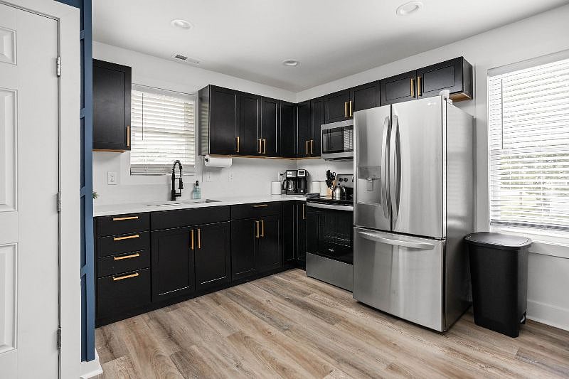 Stylish kitchen featuring black cabinetry with gold hardware, stainless steel appliances, and bright natural lighting.
