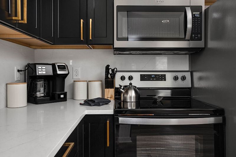 Modern kitchen with sleek black cabinetry, stainless steel appliances, and stylish gold accents.