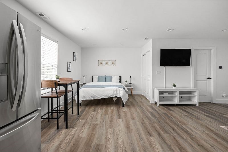 Bright and modern studio with an open floor plan, featuring a cozy bed, stylish dining area, and sleek entertainment setup.