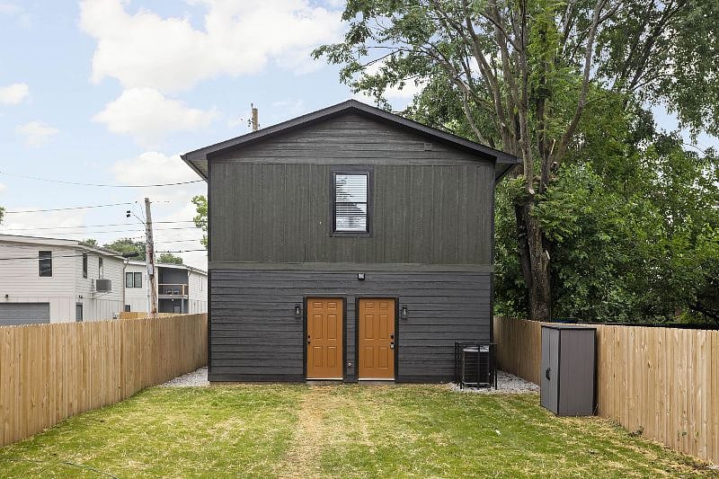 Modern duplex with a sleek black exterior, dual wooden doors, and a fenced backyard.