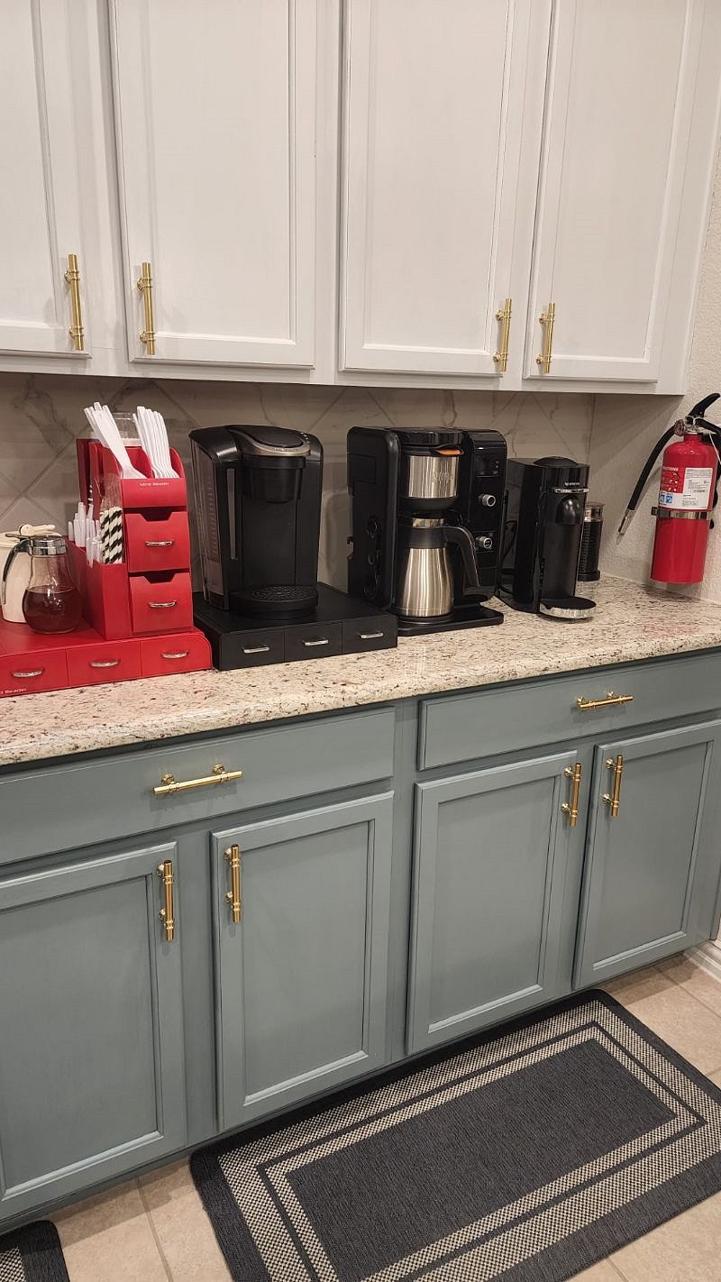 Kitchen with Keurig coffee maker with K-cups, disposable coffee cups, honey, sugar, Ninja Coffee maker, Nespresso with frother. Fire extinguisher is attached to the wall.