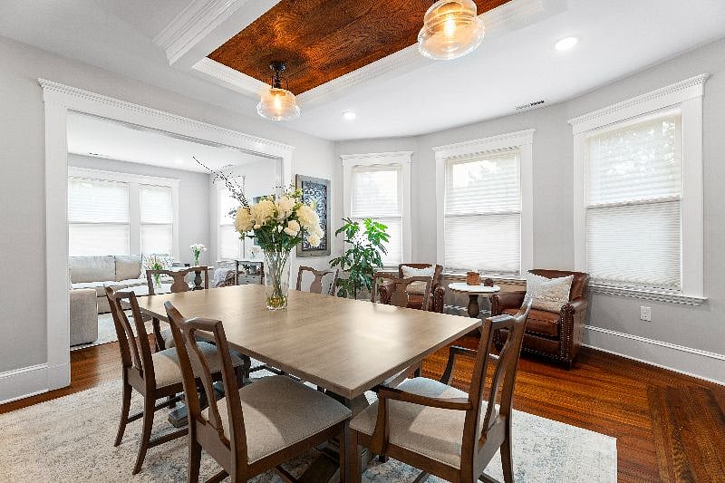 the elegant shared dining room provides an expansive space to enjoy meals or catch up on charts, featuring a large wooden dining table with seating for six, an adjacent cozy sitting nook with leather armchairs, and a stunning inset wood-paneled ceiling with warm statement lighting.