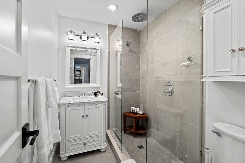 The attached private bathroom serves as a spa-like retreat after a long shift, featuring a massive glass-enclosed walk-in shower with a rainfall showerhead, a modern marble-top vanity, and bright, refreshing lighting.