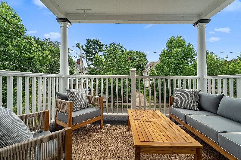 , covered outdoor porch provides a tranquil retreat to enjoy your morning coffee or fresh air before or after a long shift, completely furnished with comfortable cushioned seating, an outdoor rug, and a large wooden coffee table.