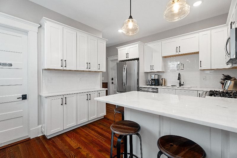 This modern, shared kitchen features bright white cabinetry, a center island with bar seating, and warm hardwood flooring.