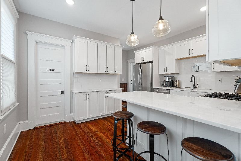 This modern, shared kitchen features bright white cabinetry, a center island with bar seating, and warm hardwood flooring.