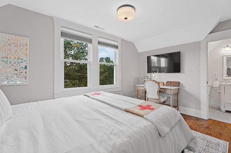 Relax in this bright, comfortable bedroom featuring a queen bed, a dedicated workspace with a desk and wall-mounted TV, and direct access to an ensuite bathroom.