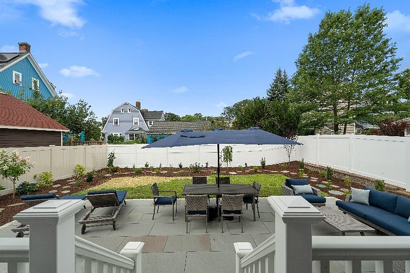 Relax and enjoy the outdoors on this spacious patio, which features comfortable lounge seating, an outdoor dining set under a large umbrella, and a well-manicured backyard area.