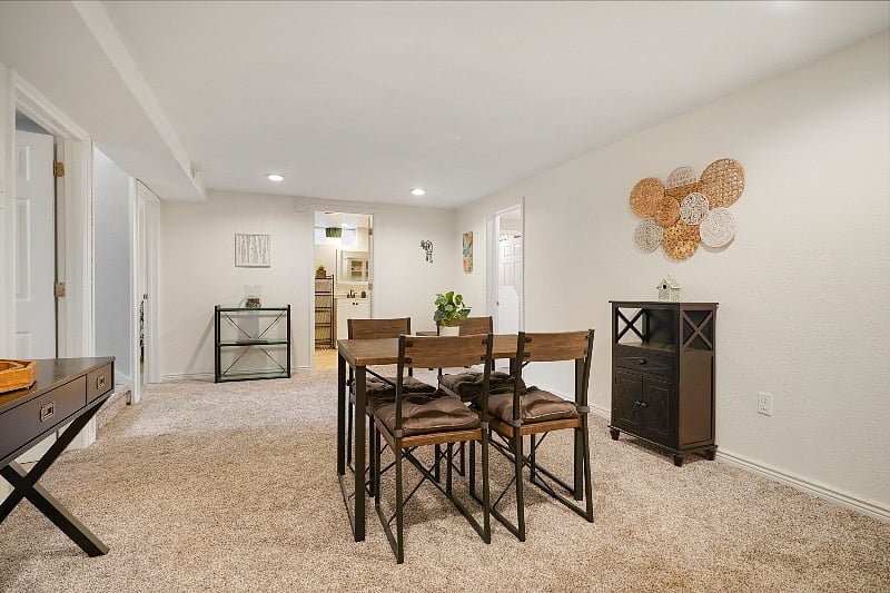 Dining area with west bedroom and kitchen doors and stairway on the left side, east bedroom on the right side, and bathroom straight ahead.