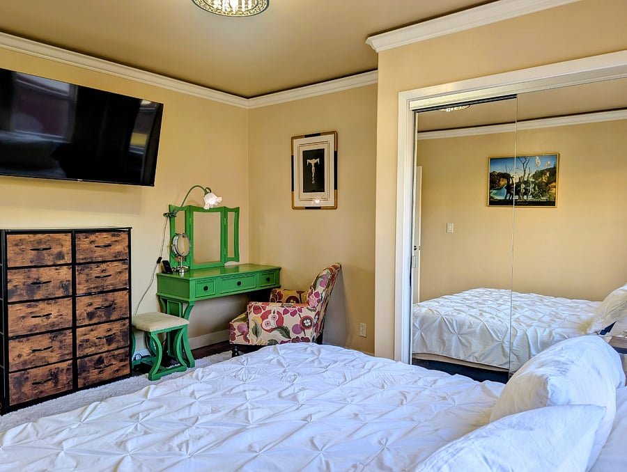 Bedroom with remote controlled adjustable king-size bed, Smart TV, full closet, 6-drawer dresser, and vanity.