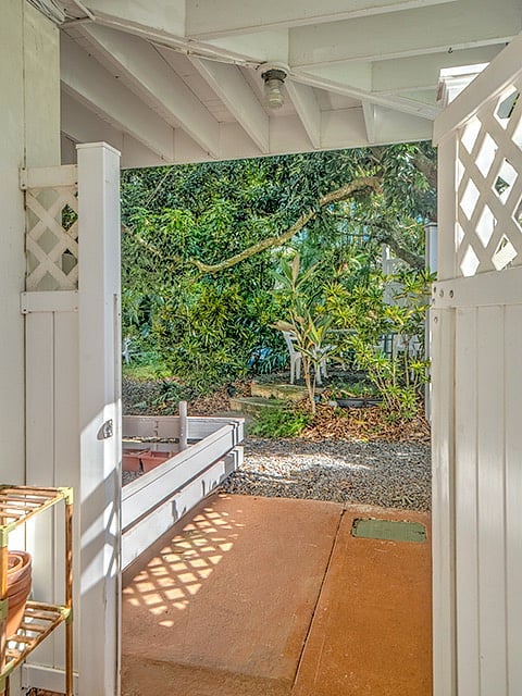 Greenery seen from the entry to the front lanai, the steps to table under the lychee tree are across the gravel path.