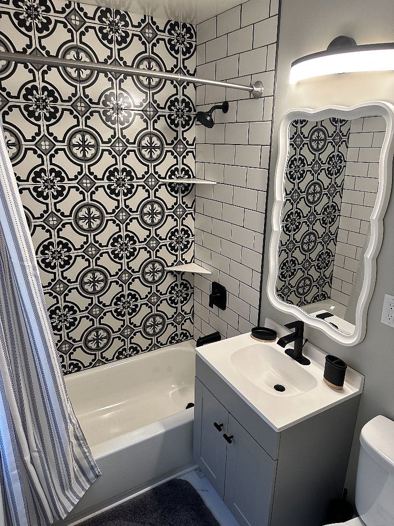 Fun bathroom features a unique mirror and tiled shower.