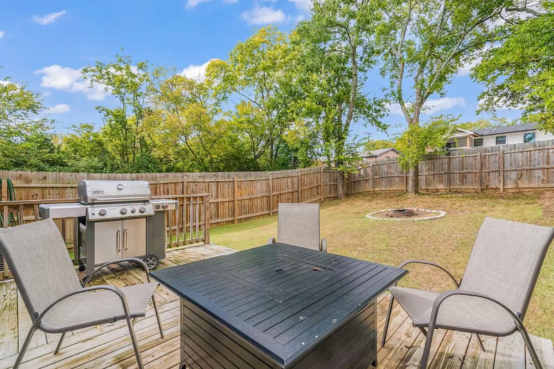 Large fenced in backyard with Outdoor Patio equipped patio furniture, 50" Smart TV, Fire Pit, Outdoor Grill, and Fire Table. 