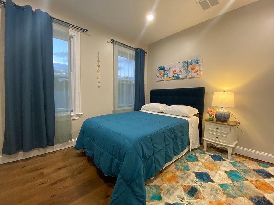 Room #2: The Sun Goddess. Large room with lots of natural light streaming from two windows. Full size bed, smart TV, nightstand, lamp, dresser, closet, and blackout curtains to reduce light and noise and to create a quiet and peaceful environment.