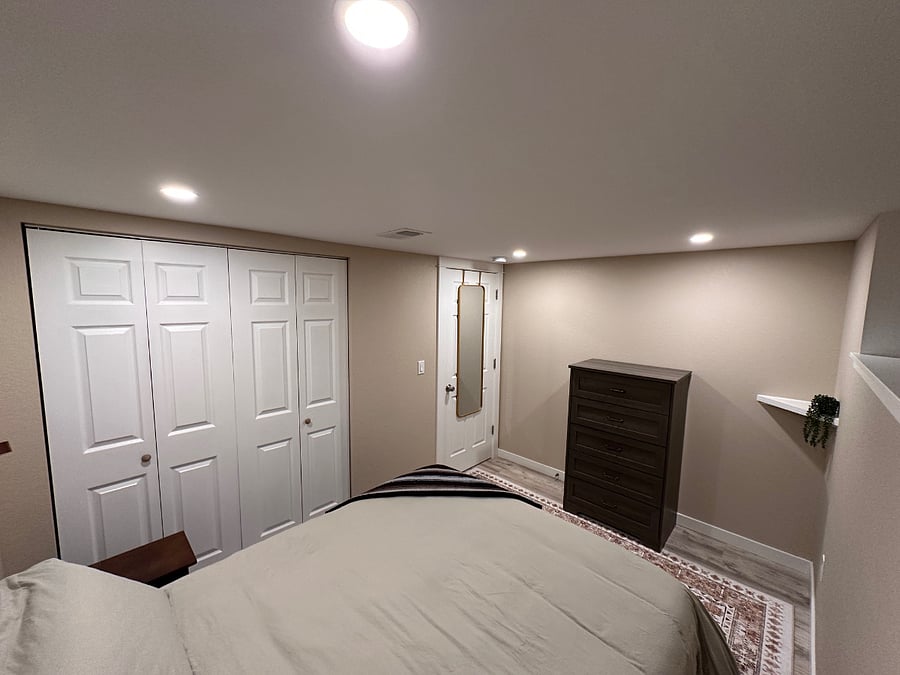 View of main bedroom from the head of the bed - showing tall 5-drawer dresser and full length mirror.