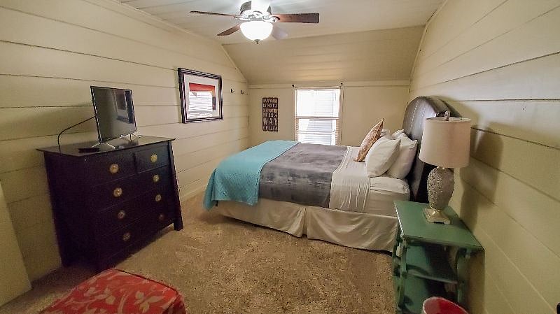 Main bedroom with California king, Roku TV, two side tables, two lamps, ceiling fan, chair with additional side table.