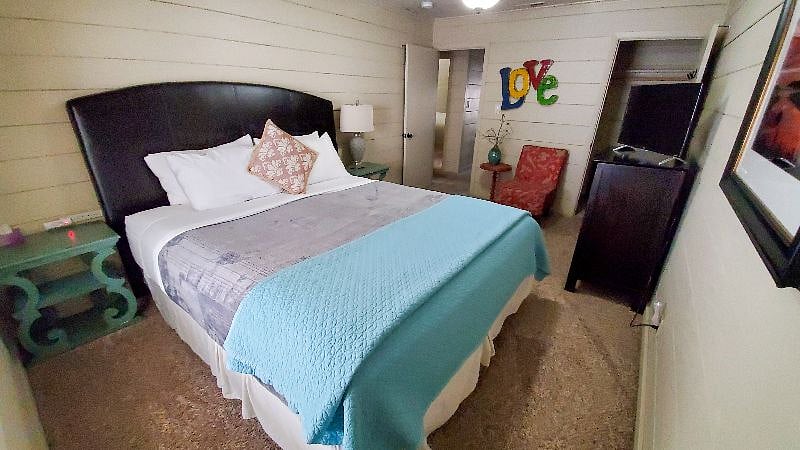 Main bedroom with California king, Roku TV, two side tables, two lamps, ceiling fan, chair with additional side table.