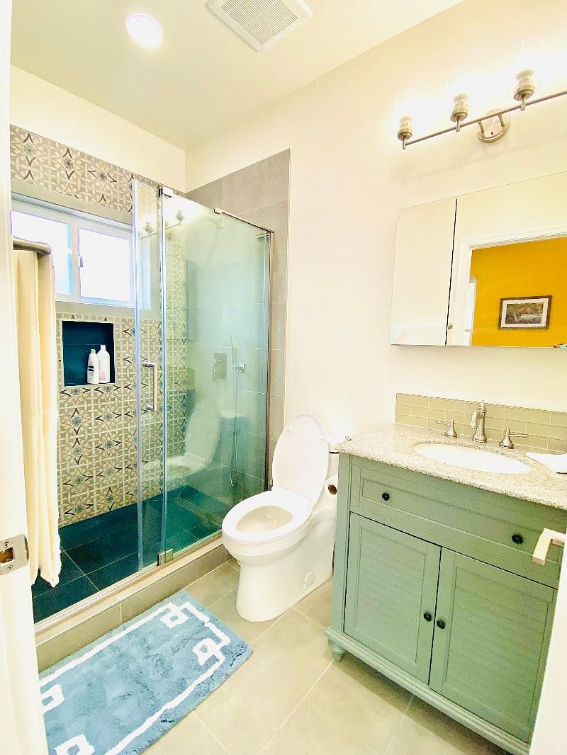 Bright bathroom with vanity lights, recessed lighting and an exhaust fan. 
Beautifully designed shower lined with mosaic tiles, a raindrop shower head with handheld and sliding glass door
