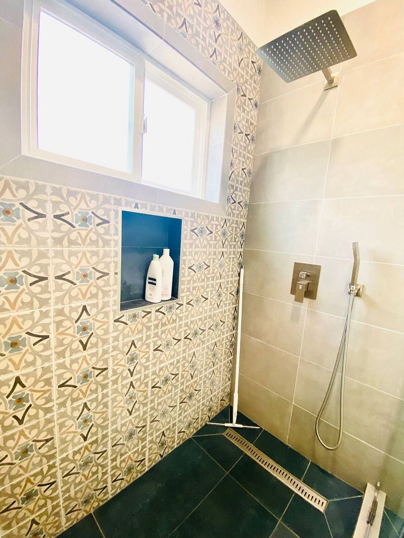 Bright bathroom with vanity lights, recessed lighting and an exhaust fan. Beautifully designed shower lined with mosaic tiles, a raindrop shower head with handheld and sliding glass door Picture taken with lights turned on here.