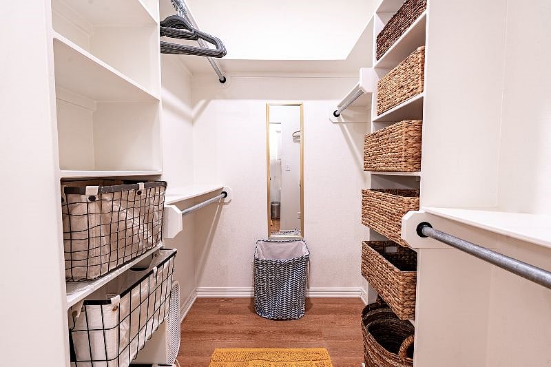 Master walk-in closet with ample storage, laundry basket, full length mirror, and full size portable fan.