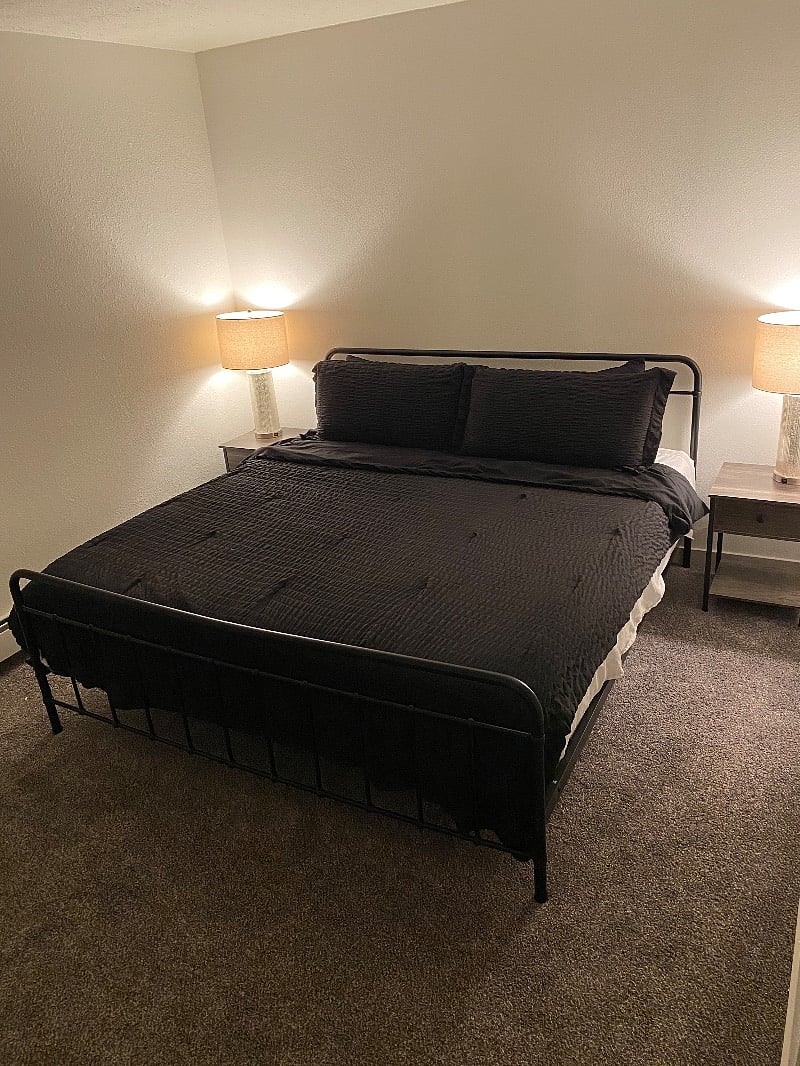 First bedroom with a king bed, blackout blinds, dresser, luggage rack and fan