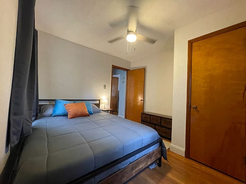Bedroom 2 with queen bed, dresser, night stand, lamp, usb charger and outlet extender, ceiling fan, black out curtains, and closet.