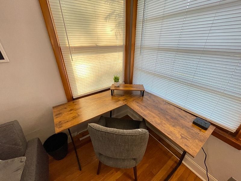 Living room with desk work space and chair, art work, coffee table, end table, tv stand, 58" TCL Google Smart TV, rug, lamps, usb charger and outlet extender, 500mbps WiFi internet, queen blanket, throw pillows, foldable futon couch for additional full-sized sleeping space, and dvd player.