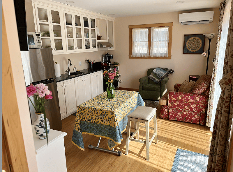 View of living area with comfortable chairs, kitchen table, and kitchen.