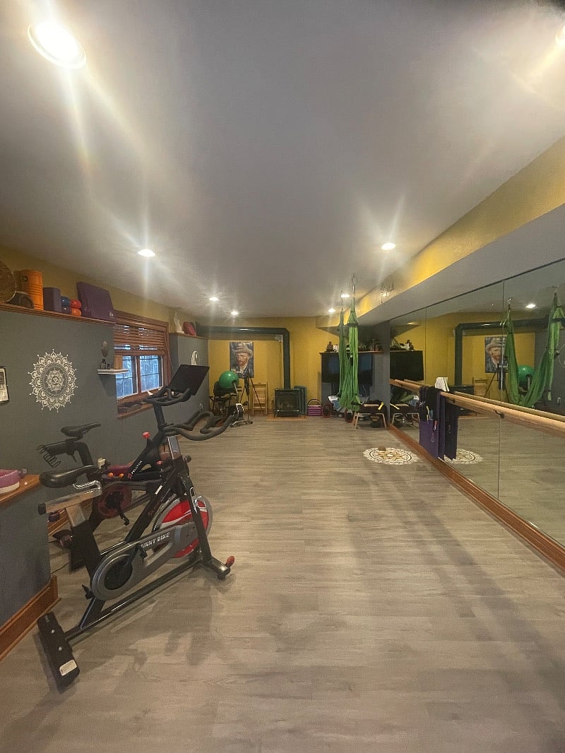 Shared gym with mirrors, ballet bar, spin bike, recumbent bike, yoga swing, yoga mats, TRX, dumbbells, weight bench and a variety of accessories.