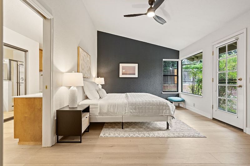 Primary suite with near black out shades on windows and on door to backyard, plus a moody feature wall with a mellow landscape photo.