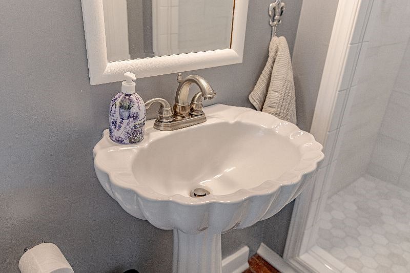 Toilet is to the left of this pedestal sink as is a window for natural light.