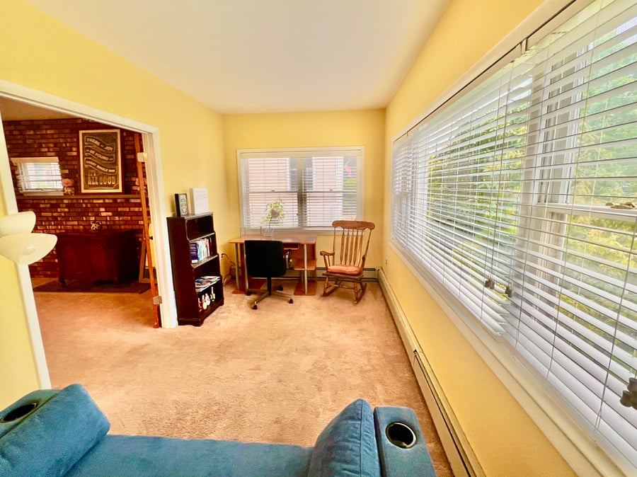 Cozy sunroom with a take a book/leave a book shelf, rocking chair, desk &lamp and couch