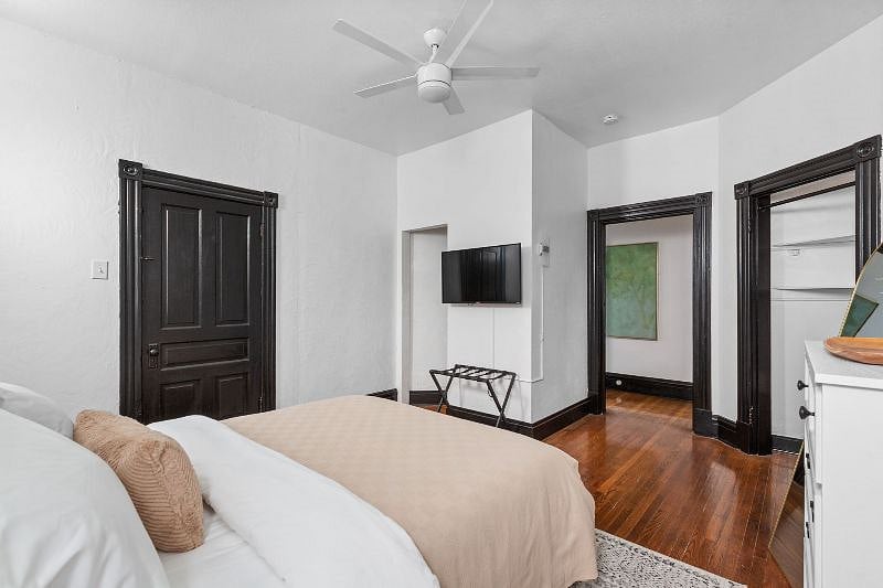 Queen Bedroom - view from window with AC unit showing (from left to right) connecting door to kitchen, walk in closet, wall mounted 40" Smart TV, luggage rack, bedroom door and corner shelf closet