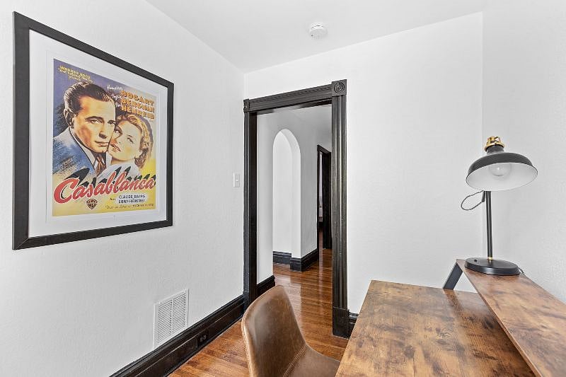 Study - view from window of workspace (desk, chair, lamp) and hallway with arched entrance into living room.