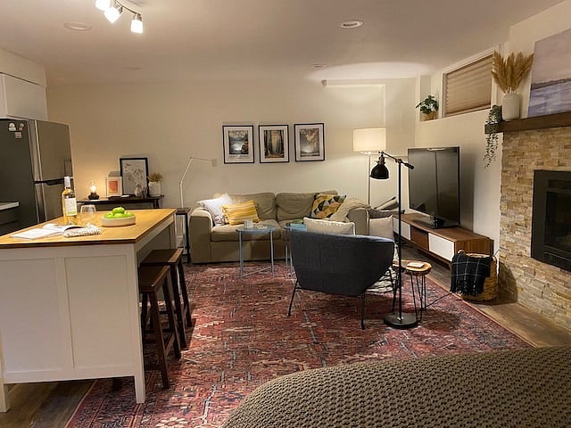 Open view of studio from queen bed of sofa, sitting chair and light and gas powered fireplace.