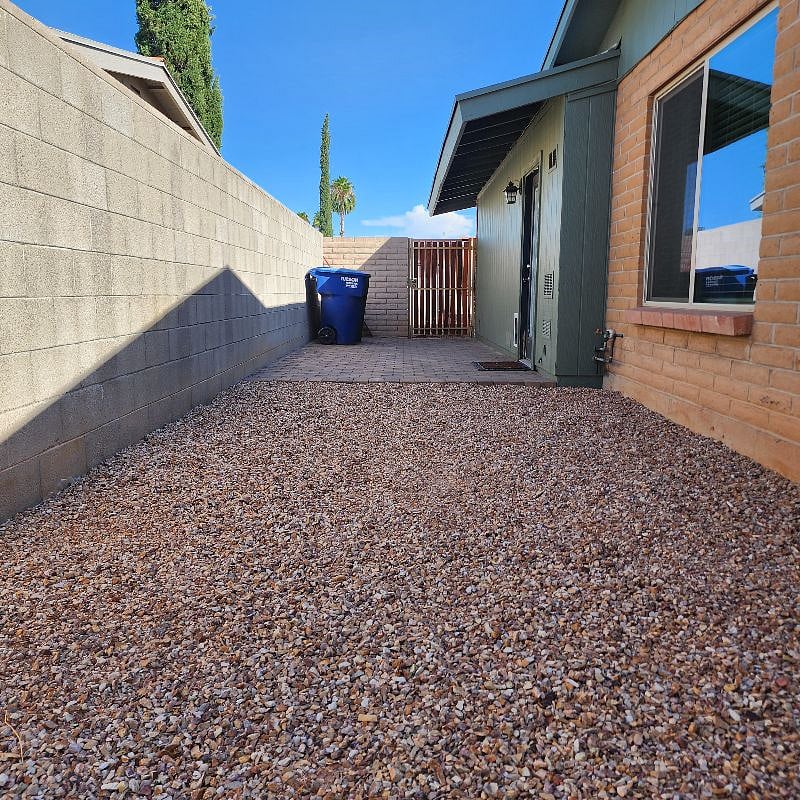 Side yard, recycle and trash bins near front driveway gate and side door to large living room.