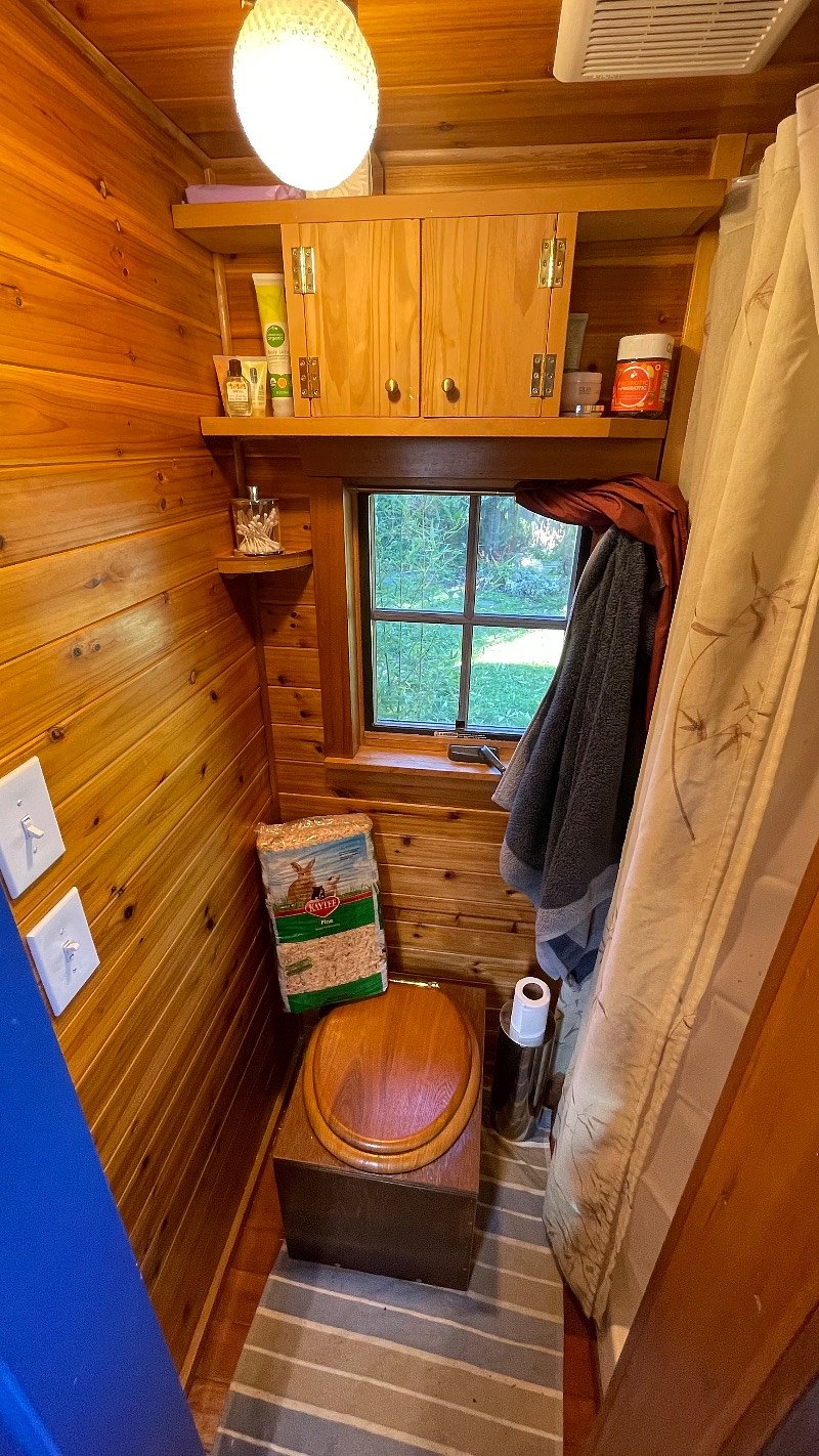 The bathroom. Composting toilet with sawdust pictured. Shower on the right. Window that opens. Fan for exhaust. 