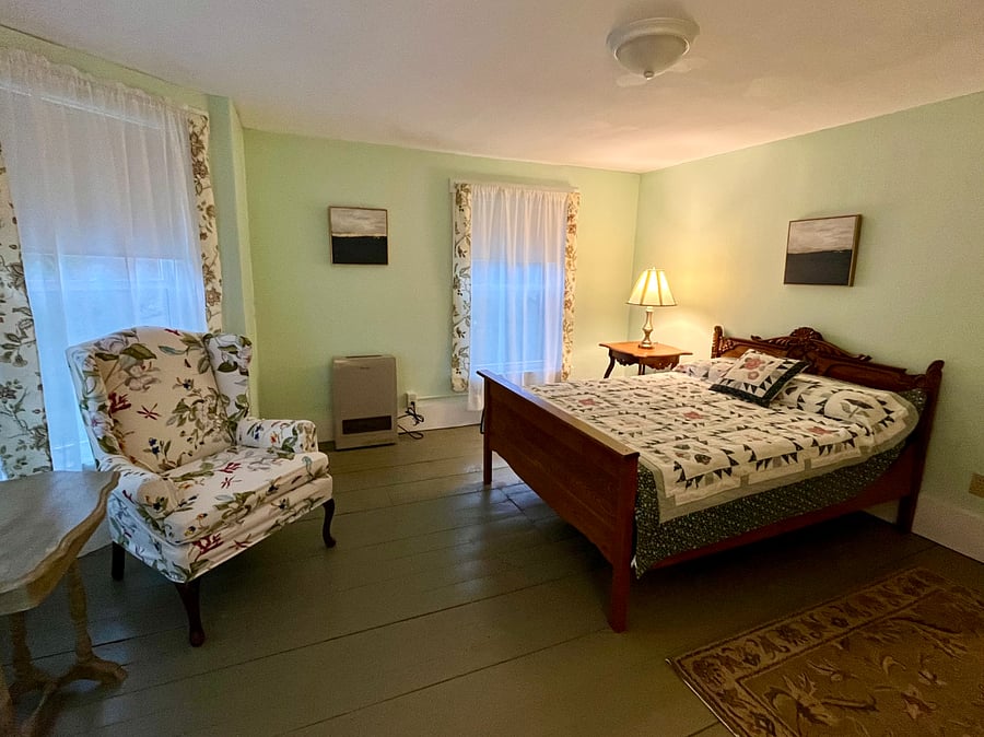 Bedroom with full-size bed and wing-back chair. Dresser, closet, and bedside table.