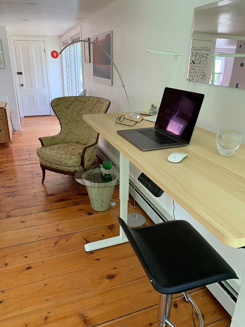 View from first-floor work area toward front door. In background, additional trestle table to the left; floor-to-ceiling windows to the right of front door.