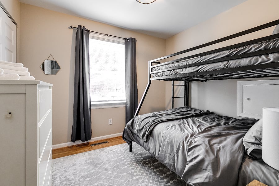 Upstairs hallway bedroom features bunkbed with full size hybrid mattress on the bottom and twin mattress on top, closet, dresser, night stand, blackout curtains, and standing floor fan.