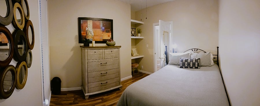 Side bedroom including shelving, five-drawer dresser, and bed lamp