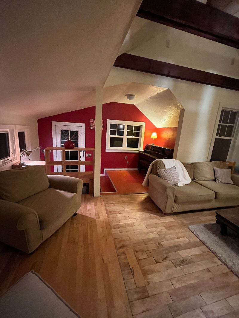 Living room has a couch and two chairs. Open format with kitchen. Out of tune piano too.