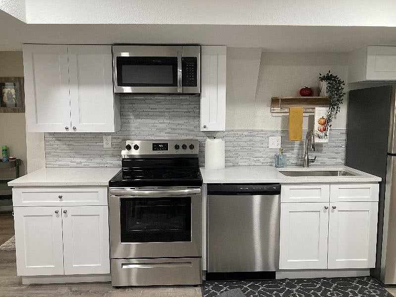 Full view of kitchen with refrigerator, electric range, oven, microwave and dishwasher. 