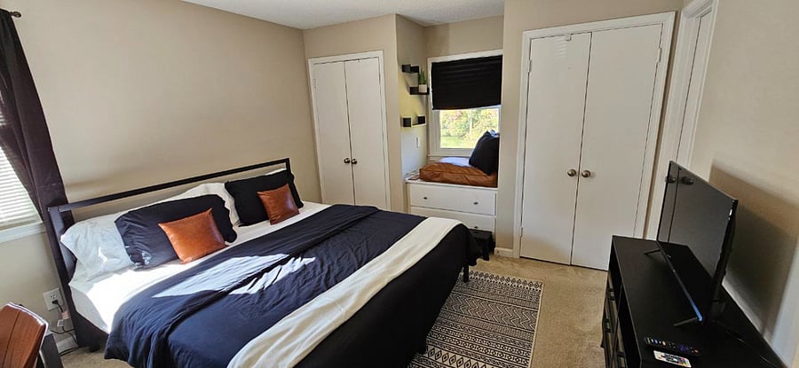 Primary Suite with a king-sized bed, cozy reading nook, flat-screen TV, desk, mirror, dresser, two closets, room-darkening/blackout curtains, and a private bathroom.